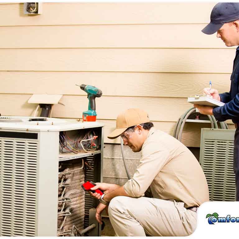 Two technicians repairing an outdoor air conditioning unit, one inspecting the interior while the other takes notes.