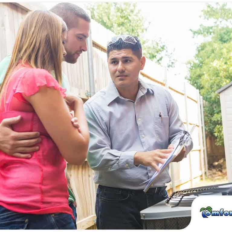A technician discusses hvac maintenance with a couple next to their home, holding a clipboard.