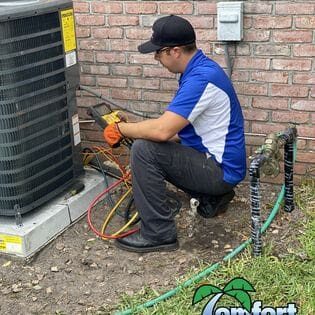 A technician in a blue and white uniform servicing an outdoor hvac unit with tools and gauges.