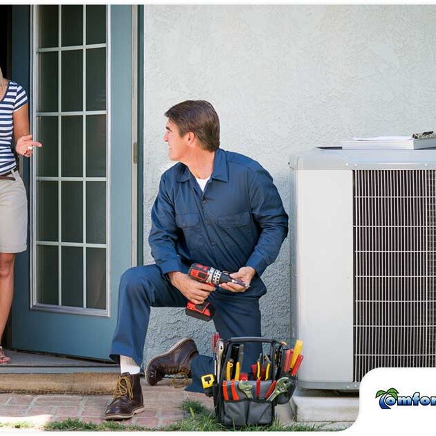 A woman talking to a male technician who is sitting next to an air conditioning unit outside a house, with tools spread on the ground.