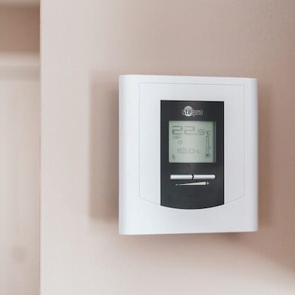A digital thermostat displaying a temperature of 19 degrees celsius mounted on a light beige wall.