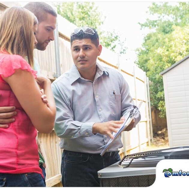 A technician discusses air conditioning unit details with a couple in their backyard, holding a document.