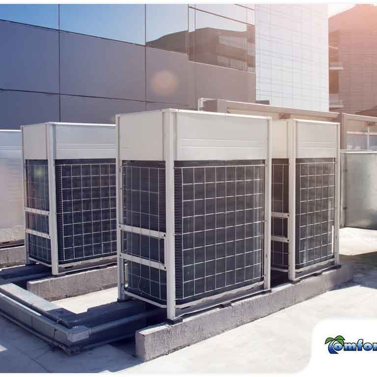 A group of industrial air conditioning units on a building rooftop under a clear blue sky.
