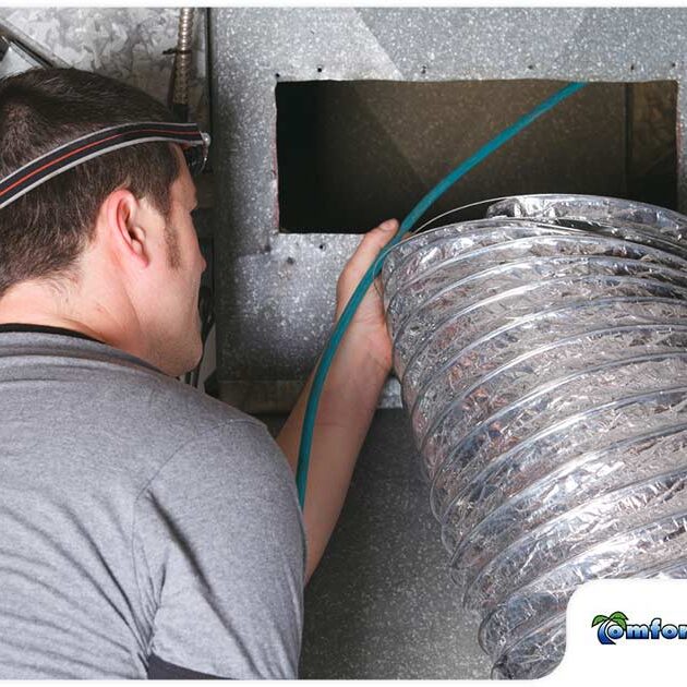 A technician installs flexible ductwork into an hvac system in a ceiling, wearing a headlamp for visibility.