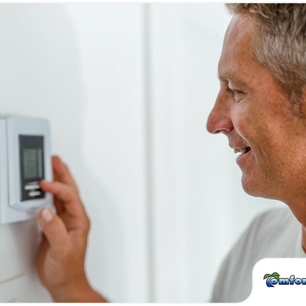 A smiling man adjusts a digital thermostat on a white wall.