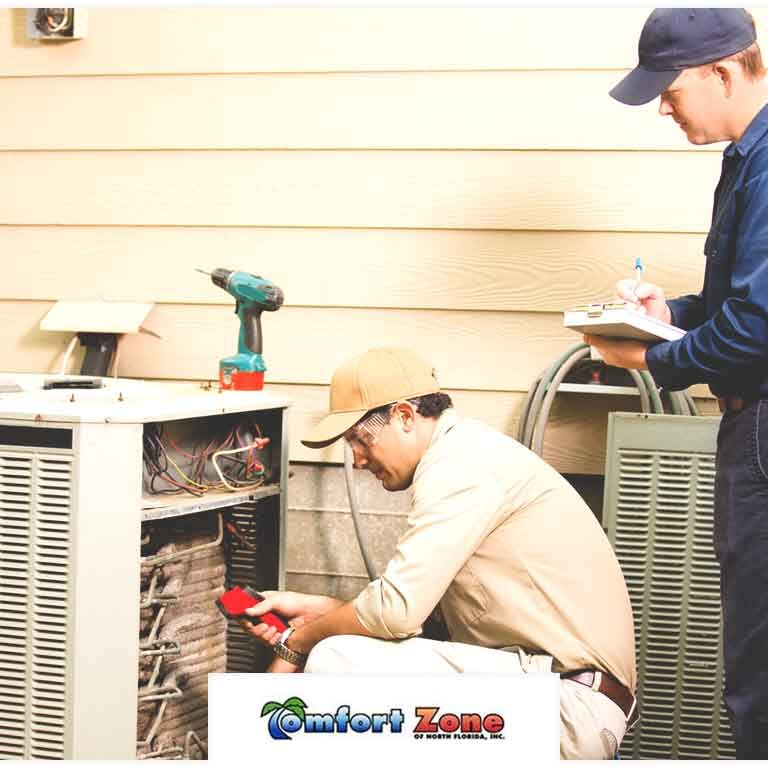 Two technicians repairing an outdoor ac unit, one working on the machinery while the other takes notes.