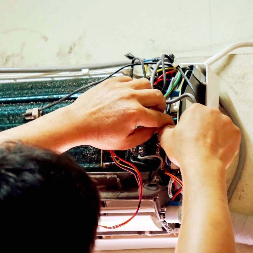 A AC Service repair technician working on wires in an indoor ductless mini split unit. A AC Service repair technician working on wires in an indoor ductless mini split unit.