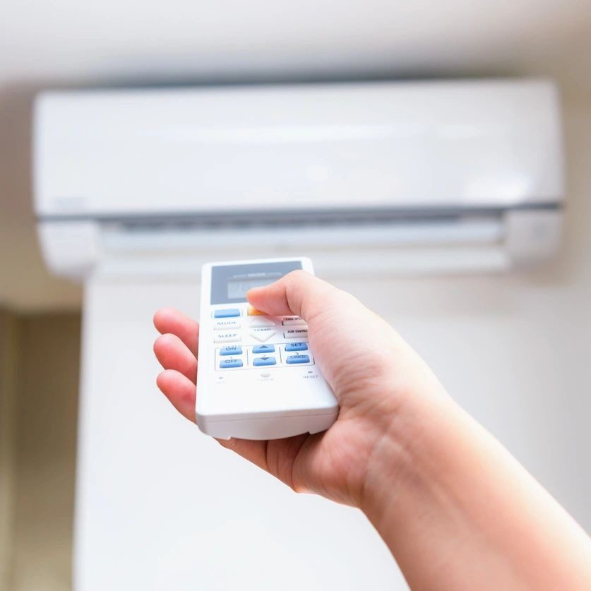 A person is holding a thermostat remote control in their hand to change the temperature on the AC system. A person is holding a thermostat remote control in their hand to change the temperature on the AC system.
