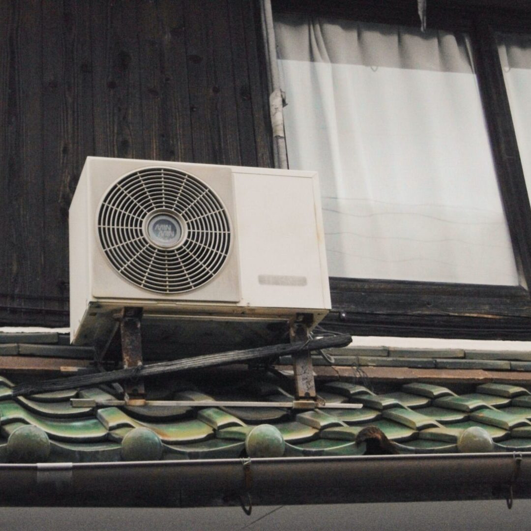 Air conditioning unit mounted on a tiled roof near a wooden window frame.