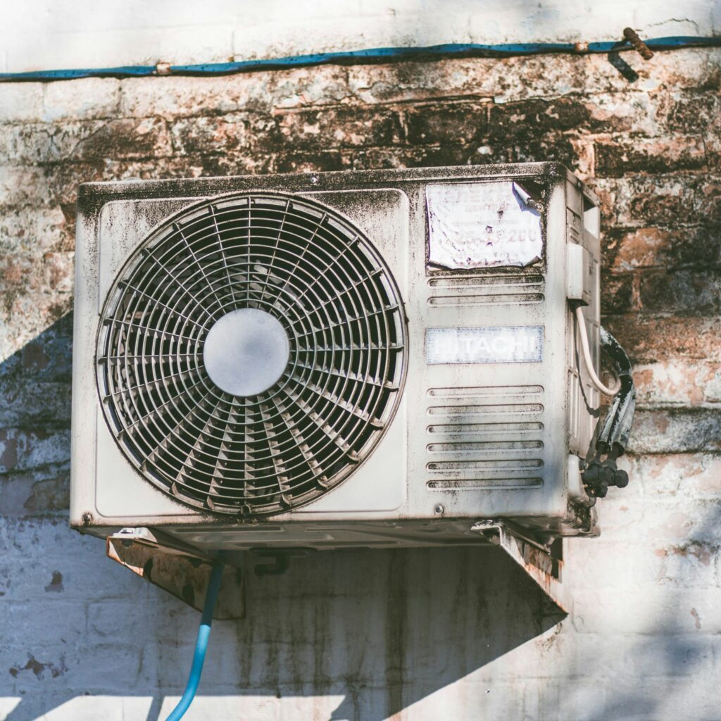 An old air conditioning unit mounted on a weathered wall with visible stains and peeling paint.